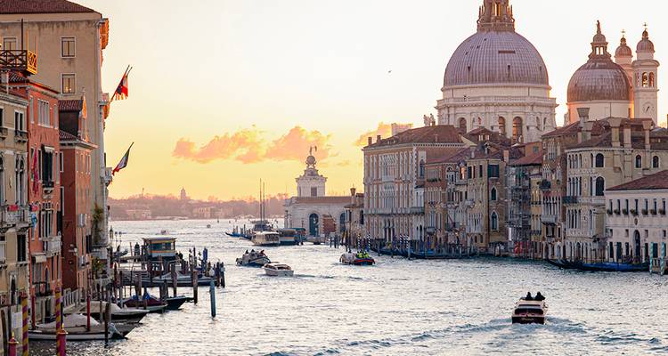 Les bateaux glissent le long du Grand Canal de Venise au coucher du soleil avec la Basilique Santa Maria della Salute en silhouette.