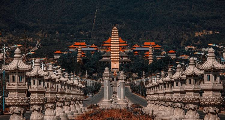 Avenida de piedra simétrica que conduce a un complejo de pagodas altas rodeado de colinas boscosas