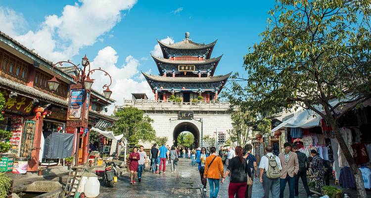 Puerta de la ciudad antigua llena de vida con turistas caminando por una calle empedrada bajo un cielo despejado
