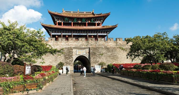 Puerta histórica de la muralla de la ciudad con tejado tradicional de pagoda, jardines y visitantes acercándose