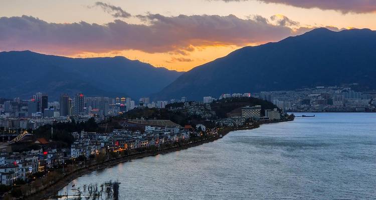 Ciudad y orilla del lago al atardecer con montañas recortadas contra un cielo naranja