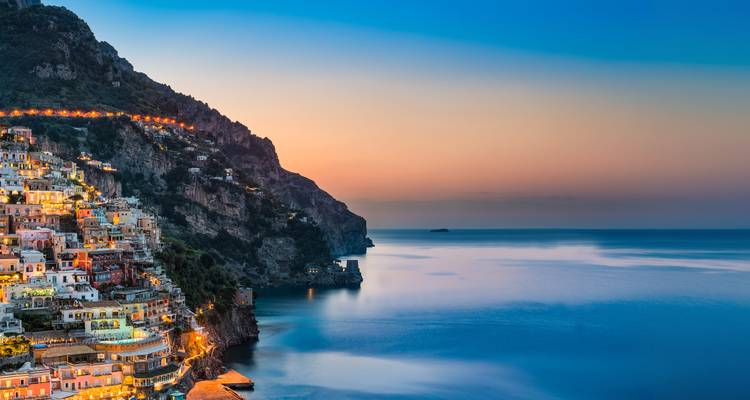 Les maisons pastel de Positano dégringolent une falaise abrupte tandis que les couleurs du crépuscule teintent la Méditerranée calme.