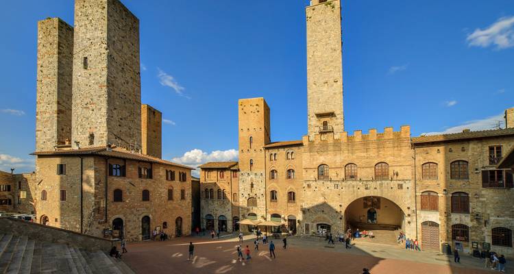 Las torres medievales de San Gimignano se alzan sobre una plaza toscana soleada llena de visitantes.