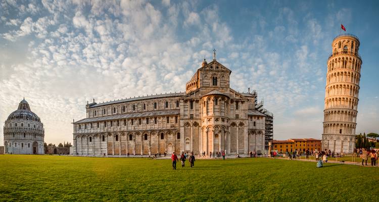 Vista panorámica de la Plaza de la Catedral de Pisa con el Baptisterio, la Catedral y la Torre Inclinada bajo un patrón de nubes dramático.