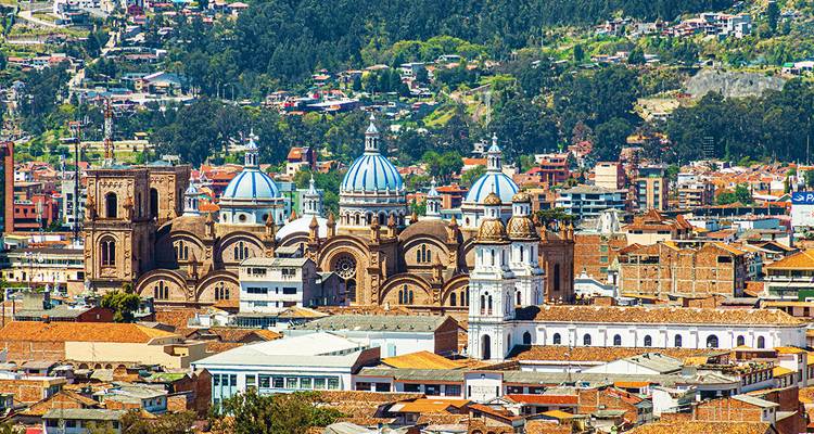 Panoramablick auf die Skyline von Cuenca mit der blaudomigen Neuen Kathedrale inmitten bunter Stadtdächer und grüner Hügel.