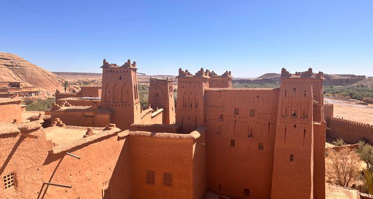 Vista elevada de los edificios de la kasbah de tierra fortificada de Ait Benhaddou bajo un cielo azul.