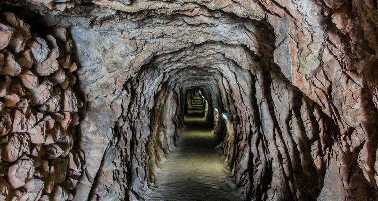 Rough-hewn underground tunnel extending into darkness with dim side lighting.