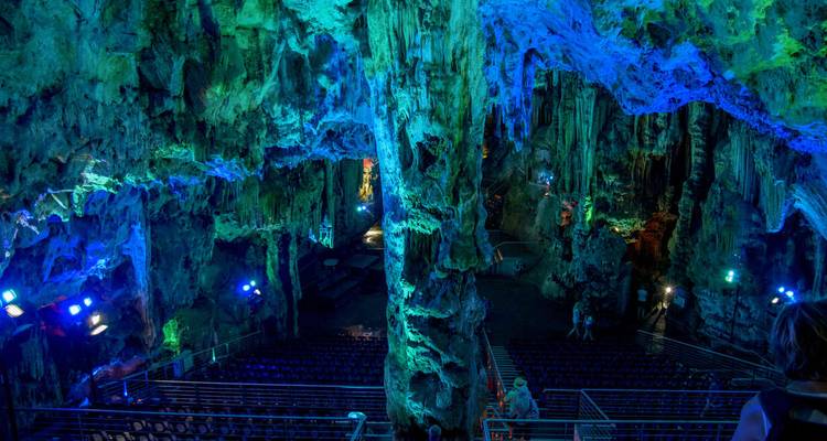 Illuminated limestone cave interior washed in blue and green light with seating set up for shows.