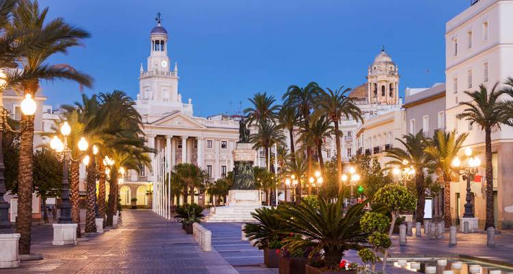 Elegant palm-lined plaza at dusk with historic buildings softly lit by golden lamps.