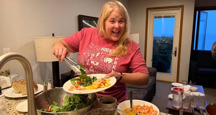 Femme souriante servant une salade fraîche dans une assiette de diner dans la cuisine accueillante d'une location de vacances au bord du lac