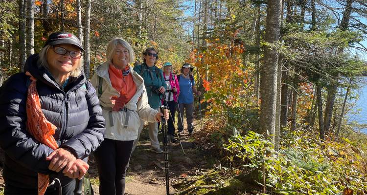 Des femmes randonneuses se tenant sur un sentier forestier étroit bordé de feuilles d'automne à côté d'un lac