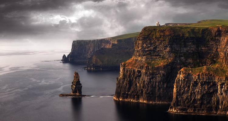 Vista aérea de clima sombrío de los espectaculares Acantilados de Moher con formación rocosa marina y la Torre de O'Brien bajo cielos tormentosos