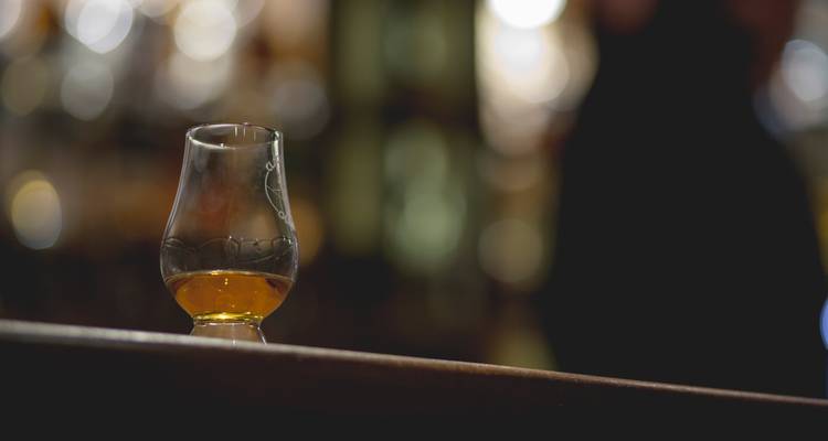 Un verre à dégustation de whisky unique contenant un spiritueux doré sur le rebord d'un bar avec un arrière-plan flou