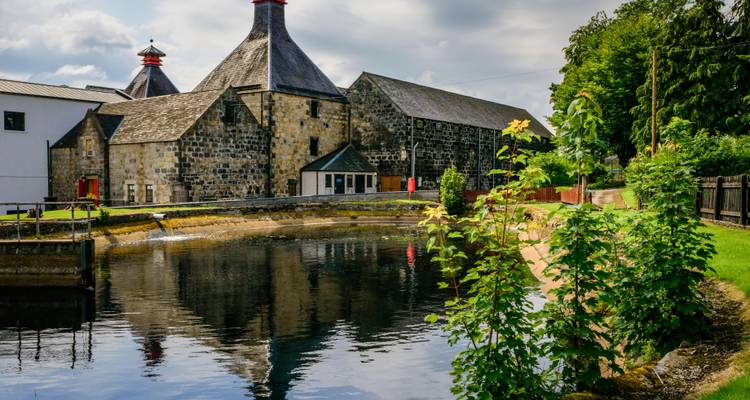 Les anciens granges à malt en pierre et les toits de pagode se reflètent dans l'étang de la distillerie entouré de verdure
