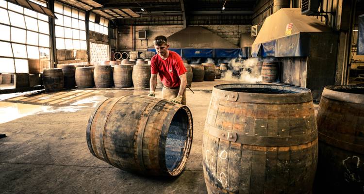 Tonnelier faisant rouler un fût de whisky fumant à l'intérieur d'un atelier traditionnel avec un éclairage dramatique chaleureux