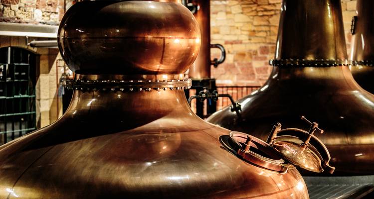Gros plan d'un alambic en cuivre brillant à l'intérieur d'une distillerie avec un mur de briques en arrière-plan