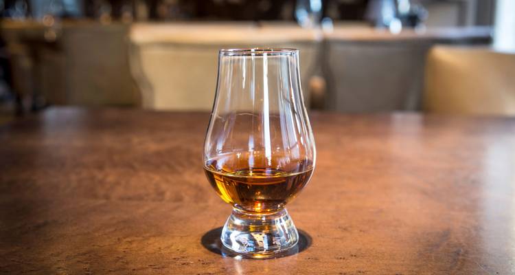 Verre de whisky unique contenant un spiritueux ambré sur une table en bois dans une salle de dégustation