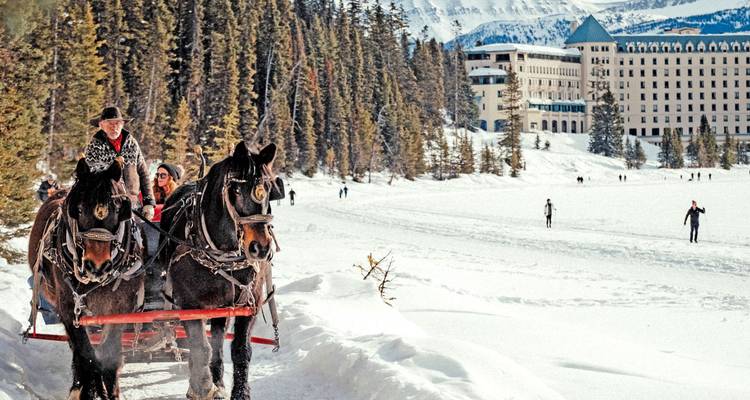 Trineo tirado por caballos que lleva pasajeros bien abrigados cruzando el nevado Lago Louise con el castillo y las montañas de fondo.