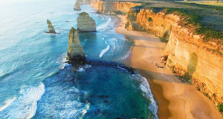 Dramatic limestone sea stacks and golden cliffs along the Great Ocean Road at sunrise.