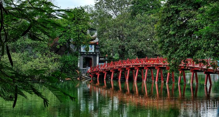 Die leuchtend rote Huc-Brücke wölbt sich über dem Hoan-Kiem-See, umgeben von üppigem Grün und einem Tempeltor.