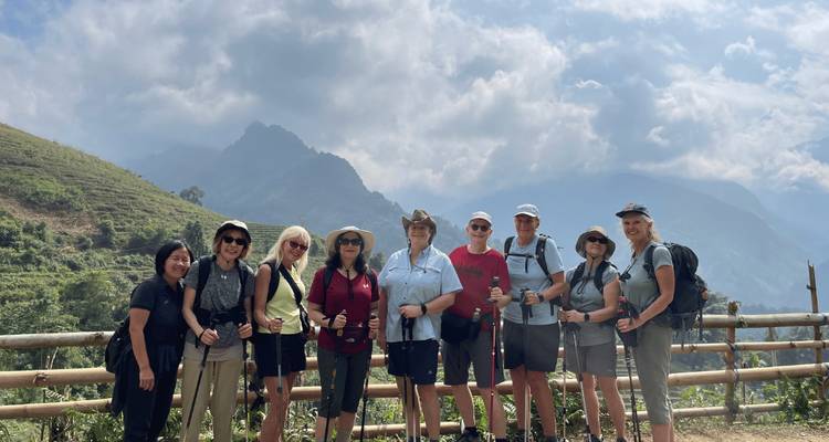Gruppe von Trekkern mit Stöcken lächelt vor dramatischer Bergkulisse und wolkenbedecktem Himmel