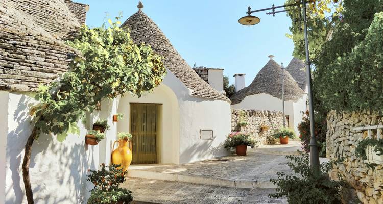 Ruhige Gasse mit charakteristischen Trulli mit Steindächern, Grünflächenakzenten und Keramikakzenten
