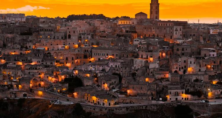 Dramatische Dämmerungsansicht über die antike Höhlenstadt Matera, die sich gegen einen orangefarbenen Himmel abhebt