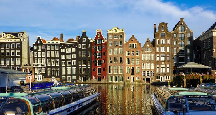 Rangée classique de maisons étroites néerlandaises au bord des canaux se reflétant dans l'eau avec des bateaux de visite à toit en verre.
