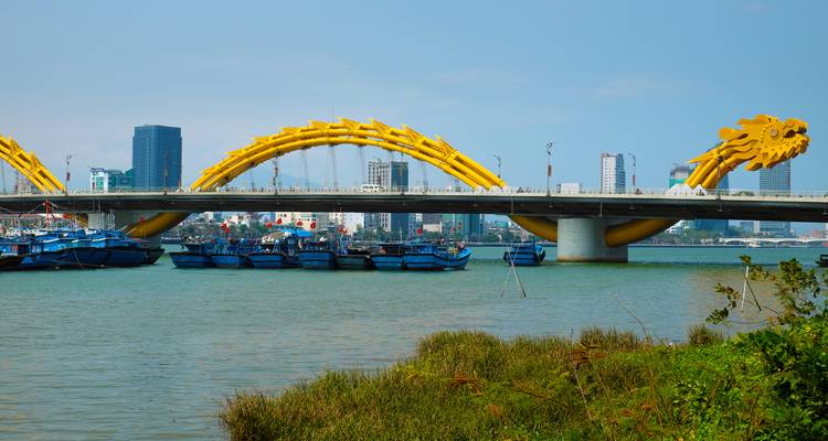 Die Goldene Drachenbrücke überbrückt einen breiten Fluss mit der Stadtsilhouette im Hintergrund