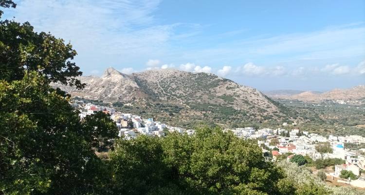 El pueblo encalado se extiende a lo largo del piso de un valle verde bajo colinas cícladas rocosas.