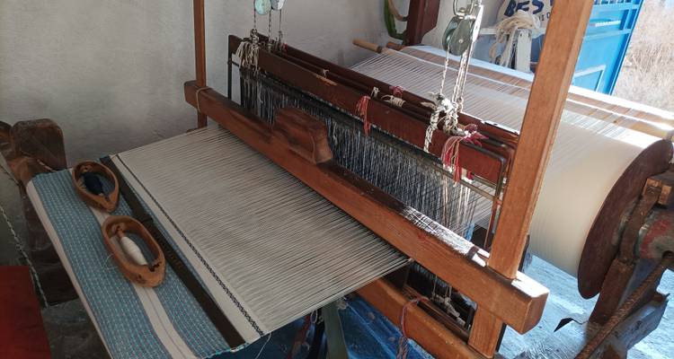 Un telar de madera tradicional con hilos de urdimbre blancos y azules cuidadosamente organizados dentro de un pequeño taller de artesanía.