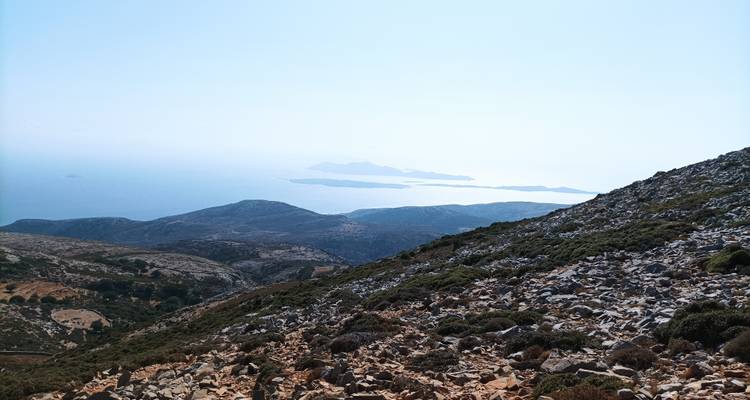 Una vista desde gran altura sobre laderas rocosas hacia islas del Egeo brillantes bañadas por la luz solar intensa.