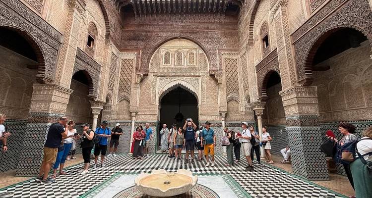 Fraai betegelde binnenplaats van een historische Marokkaanse madrasa vol toeristen die foto's maken.