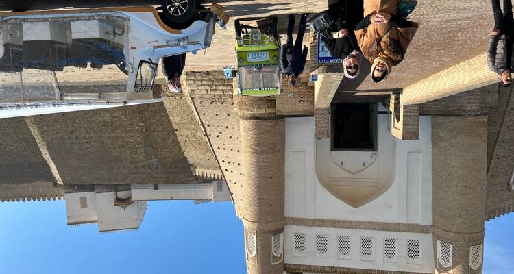Besucher, die in der Nähe der massiven Lehmwände der Artefaktfestung in Buchara stehen, mit in der Nähe geparkten Tuk-Tuks