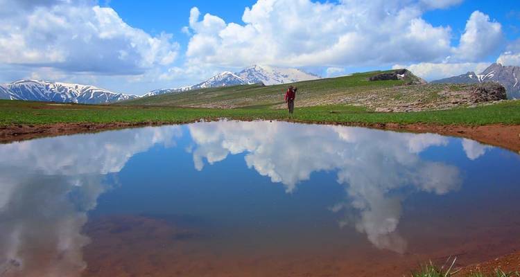 Einsamer Wanderer in der Nähe eines kleinen Bergsees, der Wolken und schneebedeckte Gipfel perfekt spiegelt