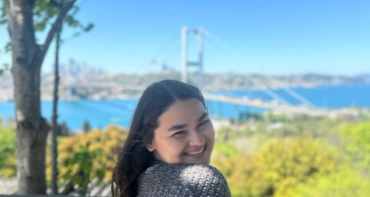 Mujer sonriente posa con el Puente del Bósforo y aguas azules de fondo.