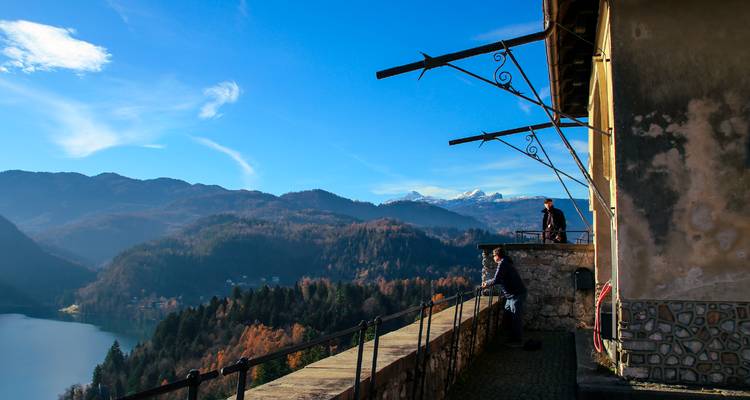Deux hommes profitant d'une vue panoramique sur les montagnes et le lac depuis une terrasse de château.