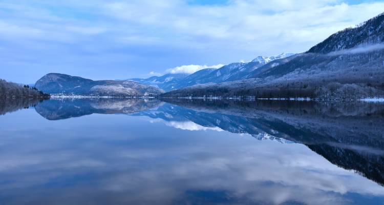Le lac Bohinj aux eaux parfaitement lisses reflétant les montagnes enneigées et le ciel d'hiver bleu.