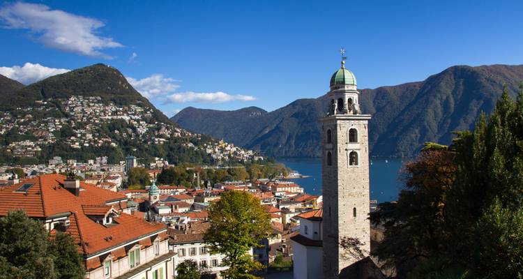 Lake Lugano view with bell tower, red-roofed town and surrounding mountains