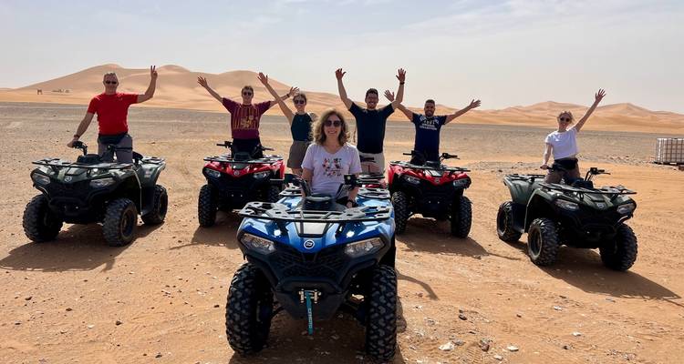 Een rij quad-rijders steekt hun armen in de lucht ter ere van het moment op een open woestijnvlakte met rollende duinen op de achtergrond.