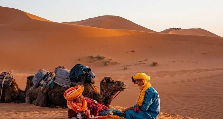 Kamelenkaravaan rust op woestijnzand terwijl twee nomaden in kleurrijke kleding in de voorgrond met elkaar praten