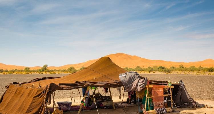Nomadische canvas tent opgezet op een kale woestijnvlakte met verre oranje duinen.