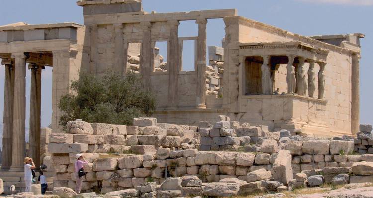 Les visiteurs explorent le temple antique de l'Erechthéion sur l'Acropole parmi les blocs de marbre usés par le temps et les oliviers.