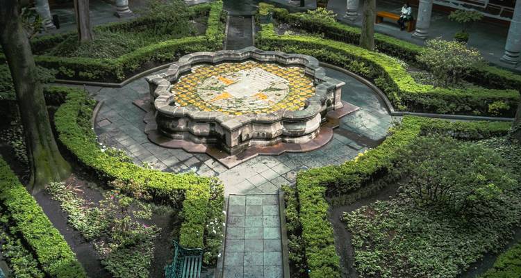 Fontaine en pierre élégante entourée de haies taillées dans un jardin de cour coloniale