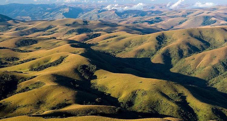 Aerial landscape of endless rolling green hills under scattered clouds in Malawi highlands.