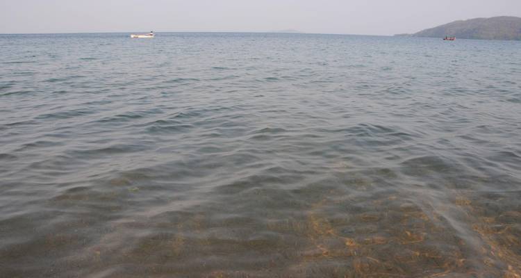 Calm, clear lake water with a small white boat in the distance and hazy green hills on the horizon.