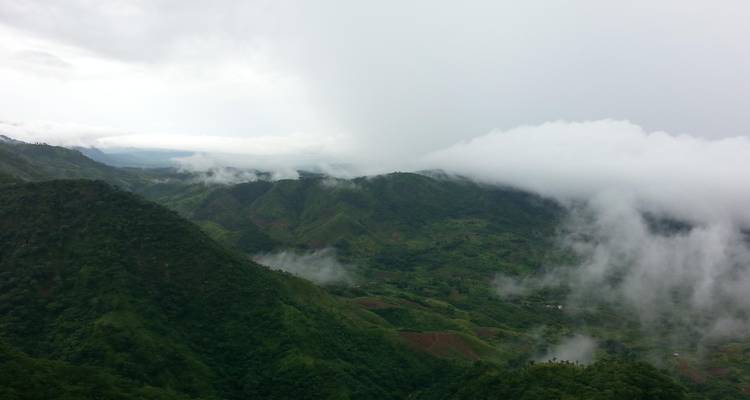 Green mountain ridges partly covered by low-hanging white clouds on an overcast day.