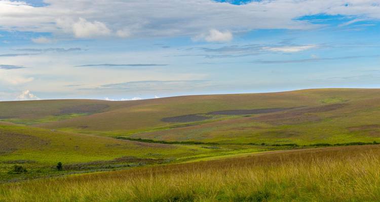 Wide expanse of rolling grassy hills under a partly cloudy blue sky.