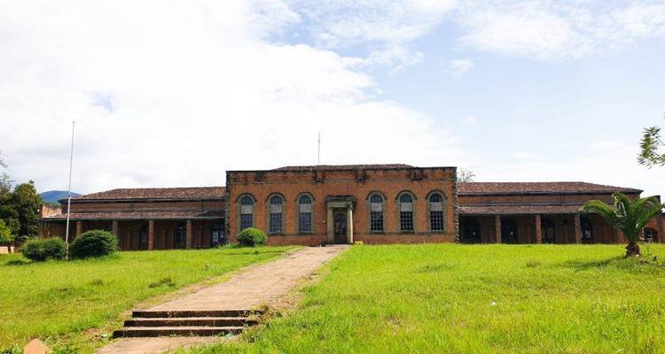 Historic red-brick colonial building set in a grassy yard with stone walkway leading to the entrance.