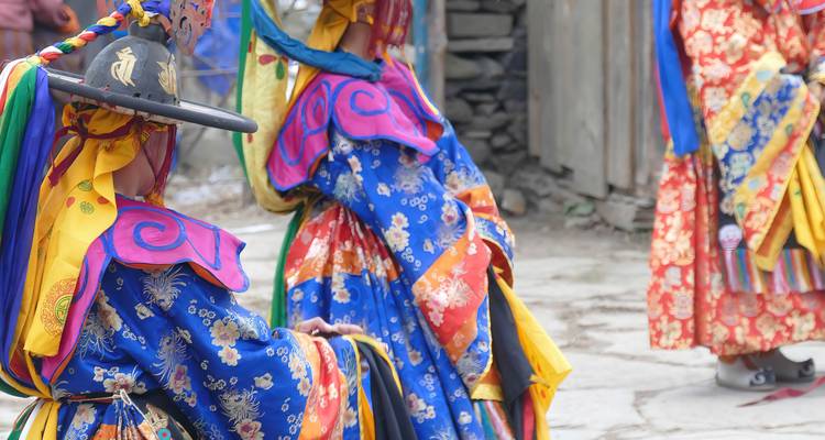 Primer plano de dos bailarines enmascarados con trajes vibrantes azul, amarillo y rojo realizando un baile festivo tradicional de Bután al aire libre.